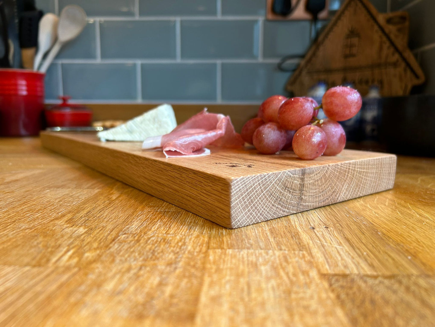 Picture of a solid oak serving platter with cheese, grapes and parma ham on top of it on a kitchen worktop