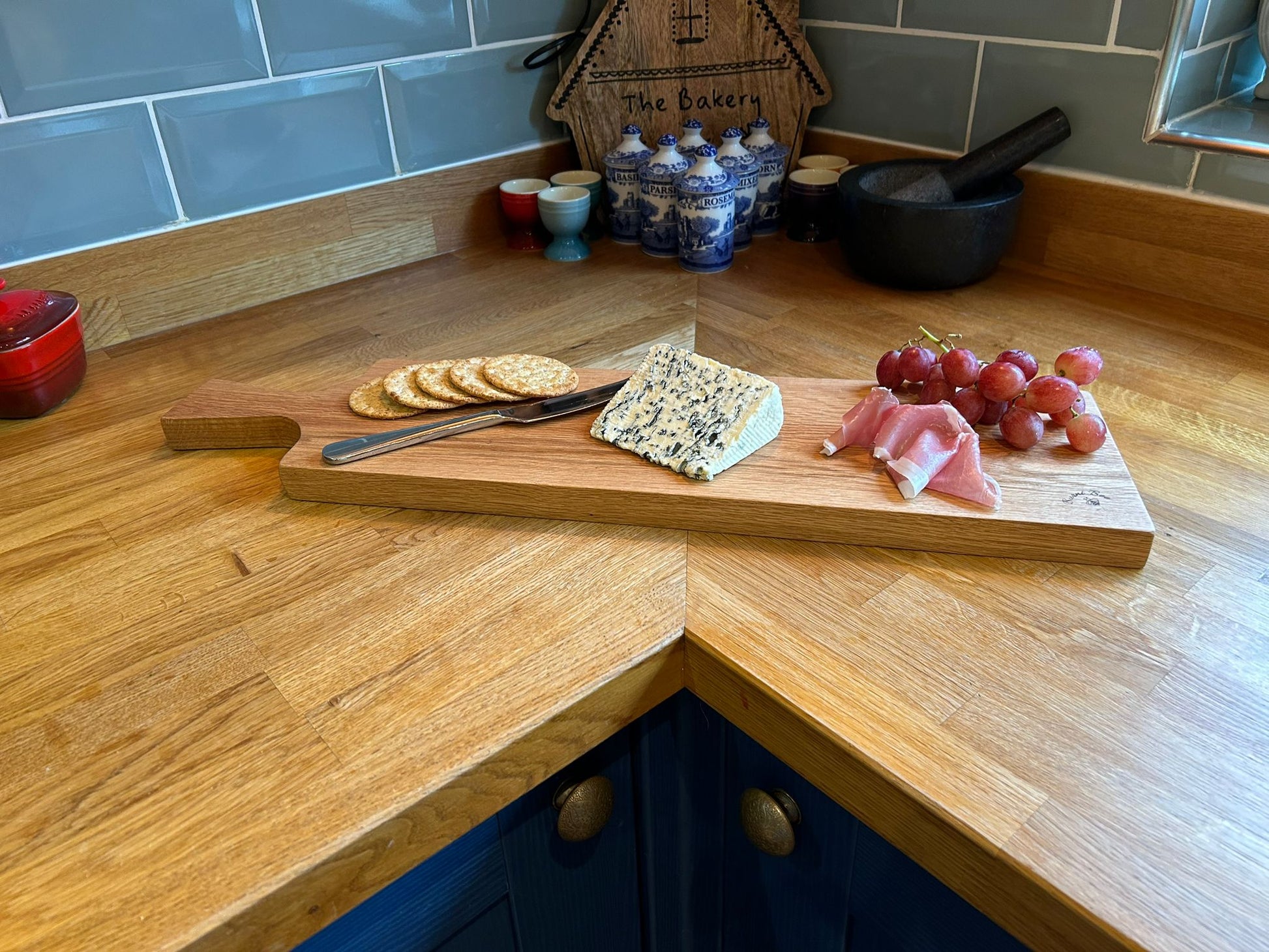 Picture of a solid oak serving platter with cheese, grapes and parma ham on top of it on a kitchen worktop