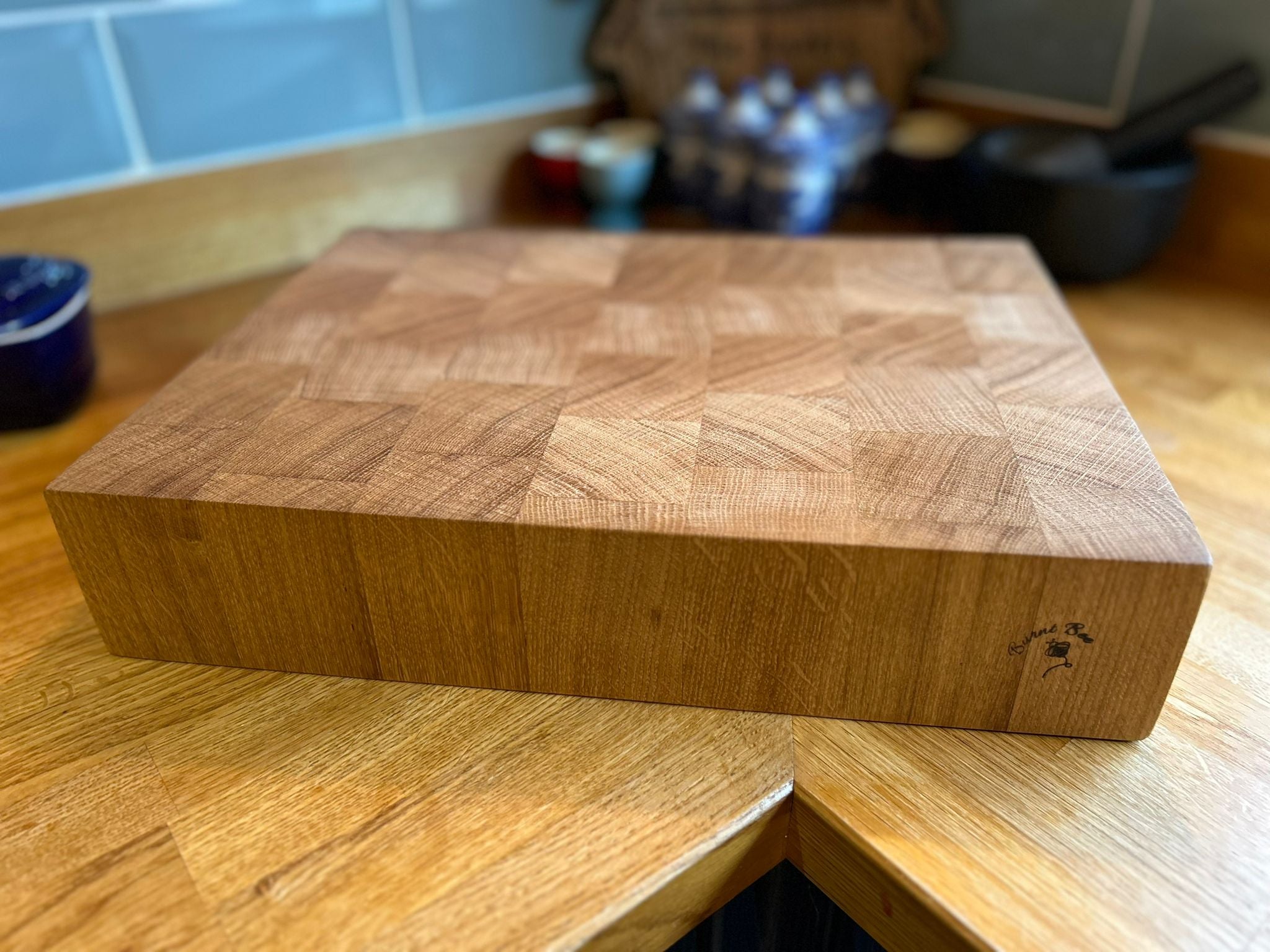 Picture of an oak end-grain butchers block with a burnt bee logo on a kitchen worktop