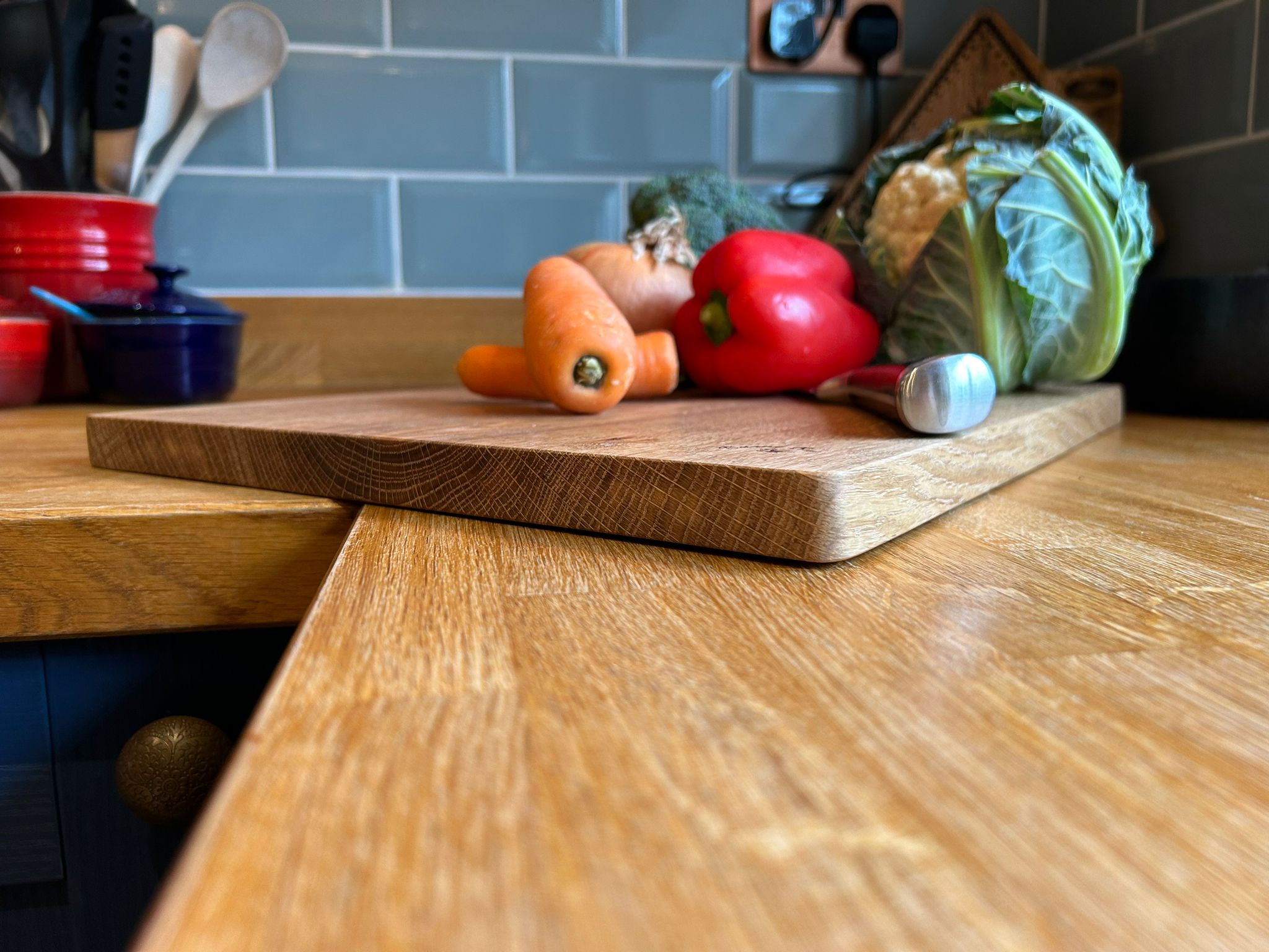 Picture of a solid oak classic chopping board with vegetables and a knife on top of it on a kitchen worktop